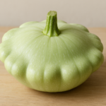 Zucchina patisson di colore verde chiaro, posizionata su una superficie di legno chiaro, che mostra la sua forma discoidale e il bordo festonato.