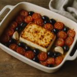 Pirofila con feta al forno circondata da pomodorini e olive, appena sfornata e dorata.