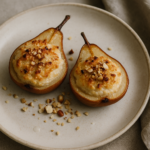 Due mezze pere Kaiser al forno ripiene di ricotta e frutta secca su un piatto di ceramica con tovagliolo di lino.