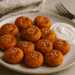 Polpette di carote dorate servite su un piatto bianco con salsa yogurt al limone a lato.