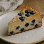 Una fetta di torta di ricotta e mirtilli con zucchero a velo su un piatto di ceramica.