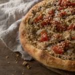 Una focaccia manaqish bi kishk con condimento di yogurt, pomodoro e cipolla, servita su un tavolo di legno.