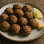 Polpette di sarde dorate servite su un piatto di ceramica rustico con spicchi di limone.